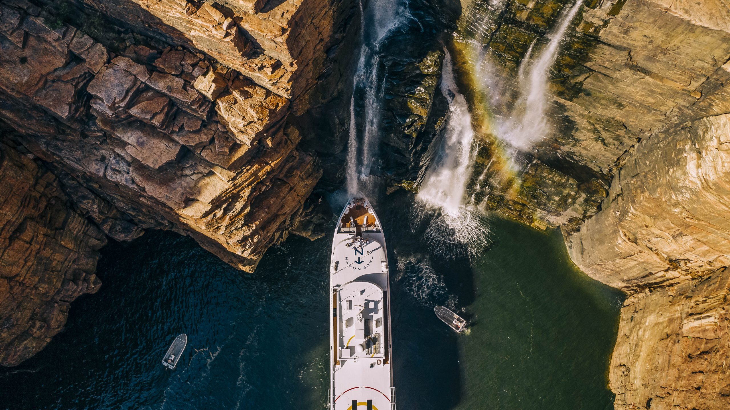 Aerial view of True North luxury cruise ship at majestic Kimberley waterfall.