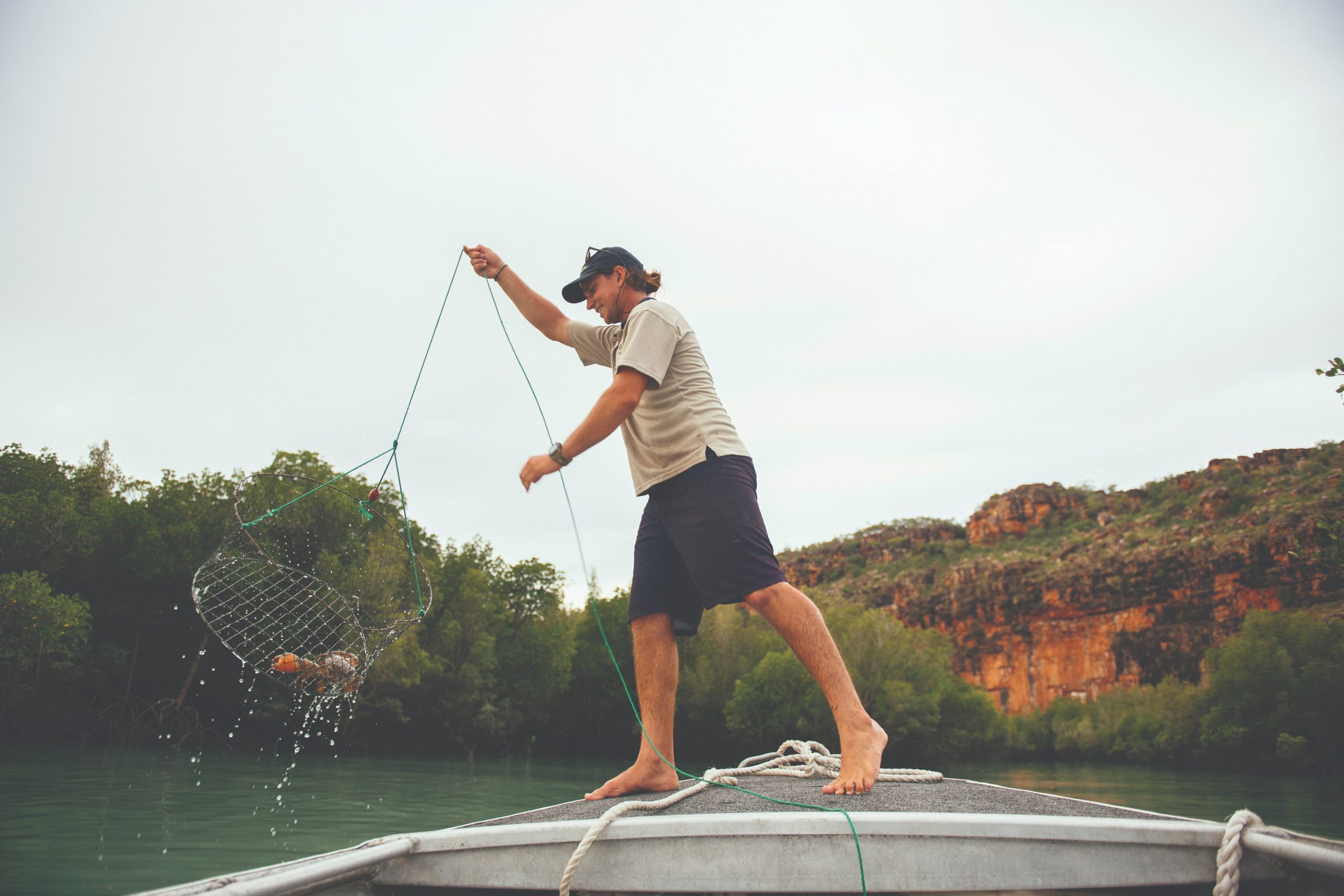 A barefoot guest aboard a small adventure tender hauls up a crab pot from turquoise waters during a TRUE NORTH Kimberley expedition cruise. 