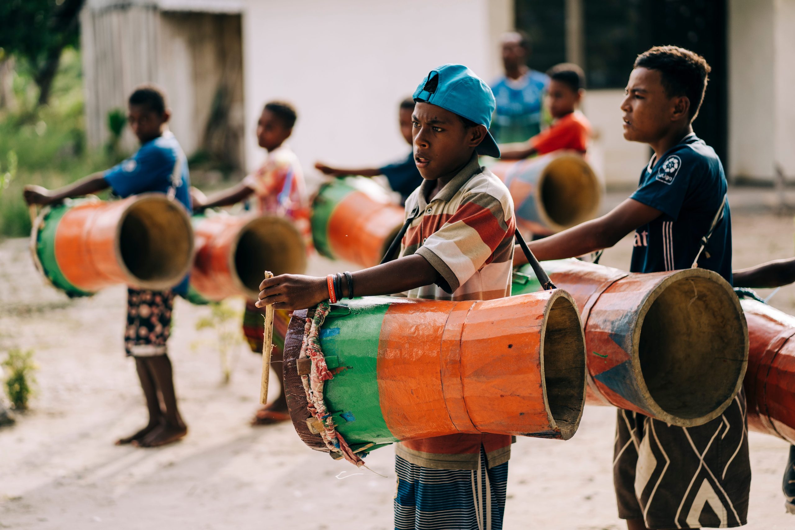 A group of young boys in Raja Ampat playing large, brightly painted traditional drums