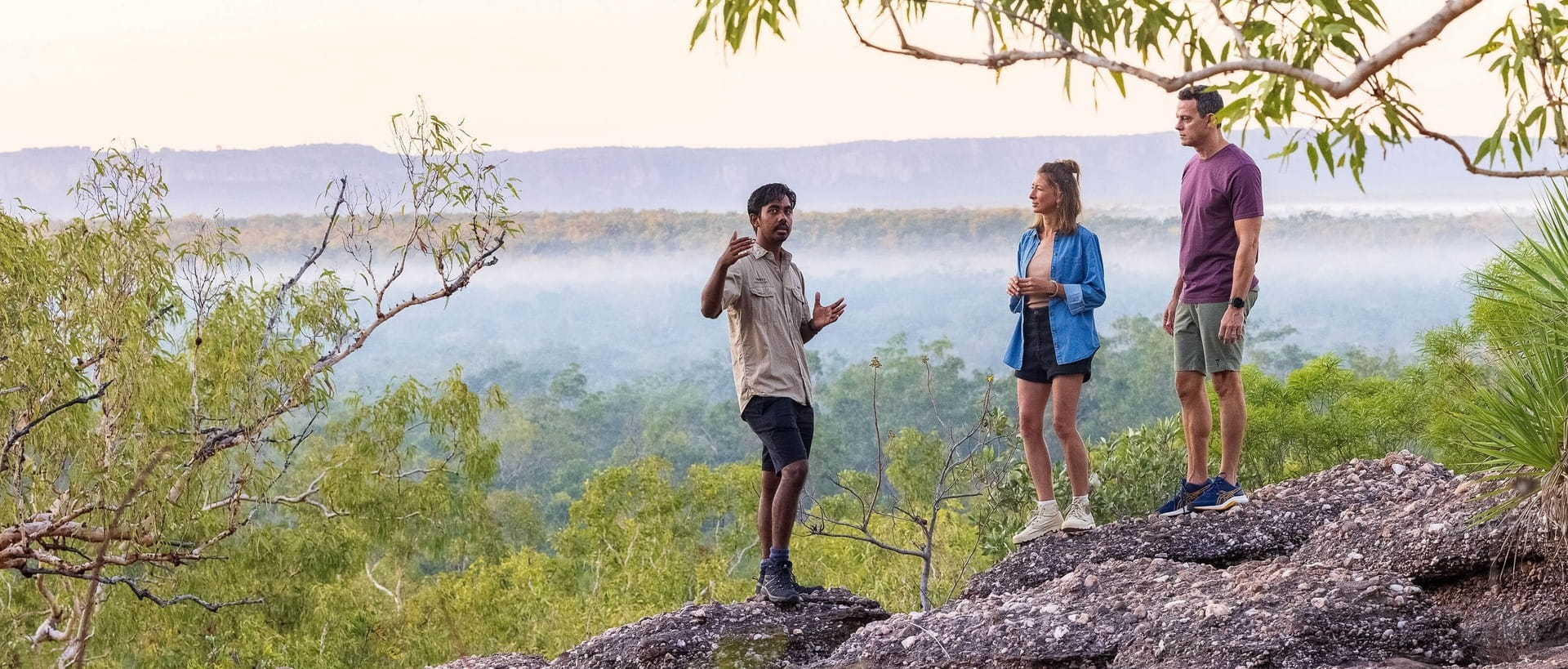 Two travellers listen as a guide explains the surroundings during a wilderness expedition.