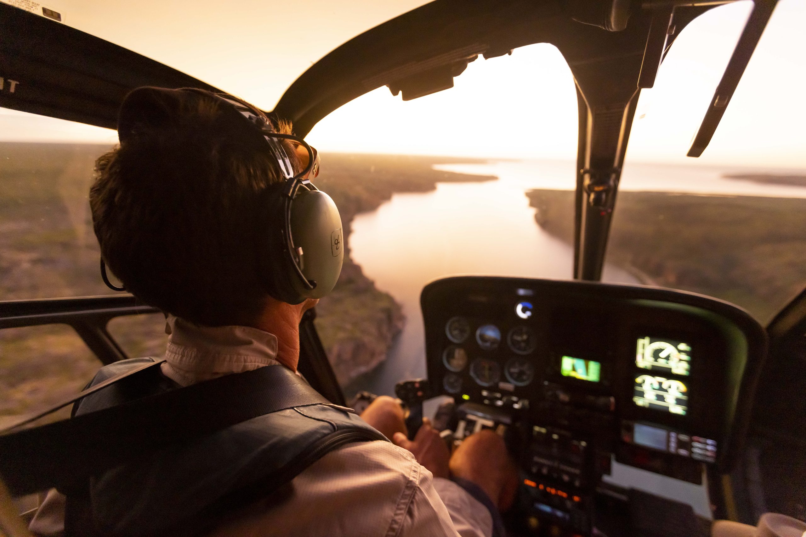 Pilot in a helicopter flying over a winding river at sunset, capturing the scale and remote beauty of Australia’s landscapes from above during a True North expedition