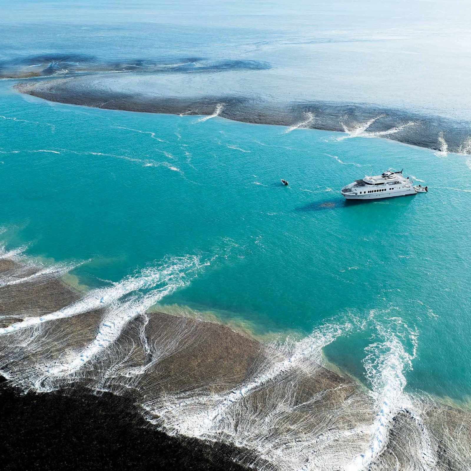 Aerial view of a ship in turquoise water beside a tidal sandbank
